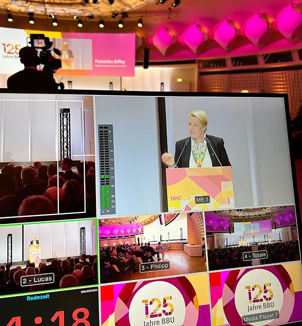 A conference event with a speaker on stage, multiple camera views, and '125 Jahre BBU' on the screen.