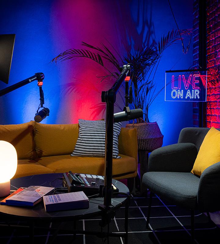 Movact Studio Berlin setup with yellow and gray chairs, microphones, and a 'Live On Air' neon sign.