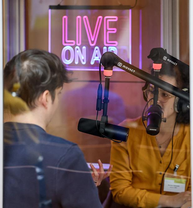 Podcast recording session with two people and a LIVE ON AIR neon sign in the background.