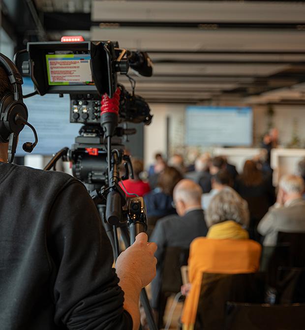 A cameraman recording a conference or presentation with an audience in the background.